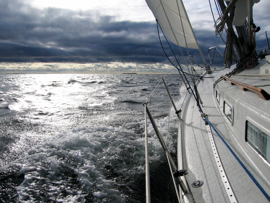 Ongoing sailing in windy conditions, looking forward towards dark clouds with the sun shining through.