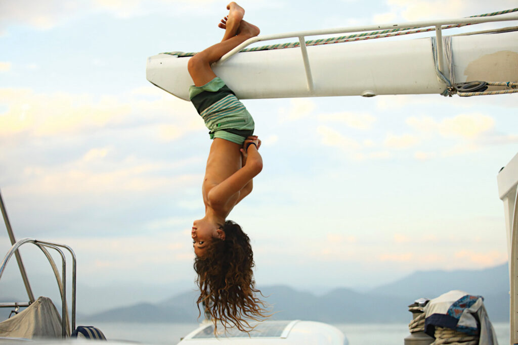 child hanging upside down from boat mast