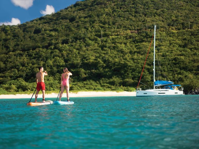 Couple paddle boarding near an anchored sailboat