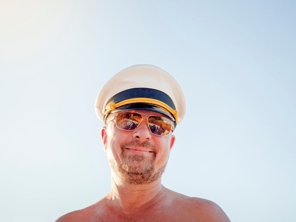 Funny mature bearded captain without a shirt resting on vacation in a resort on the sky background