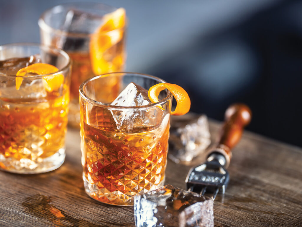 Old fashioned rum drink on ice with orange zest garnish.